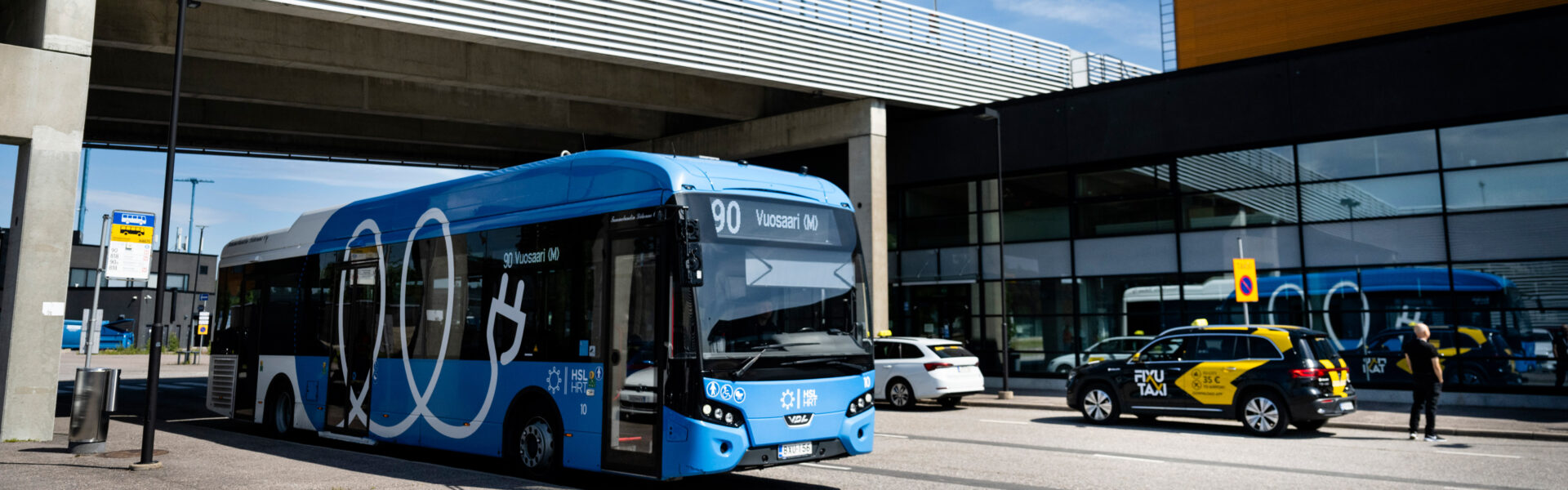 A buss and a taxi in front of a passenger terminal.